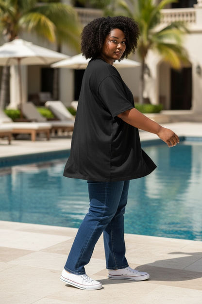 Woman in black oversized shirt and blue jeans standing by a poolside.