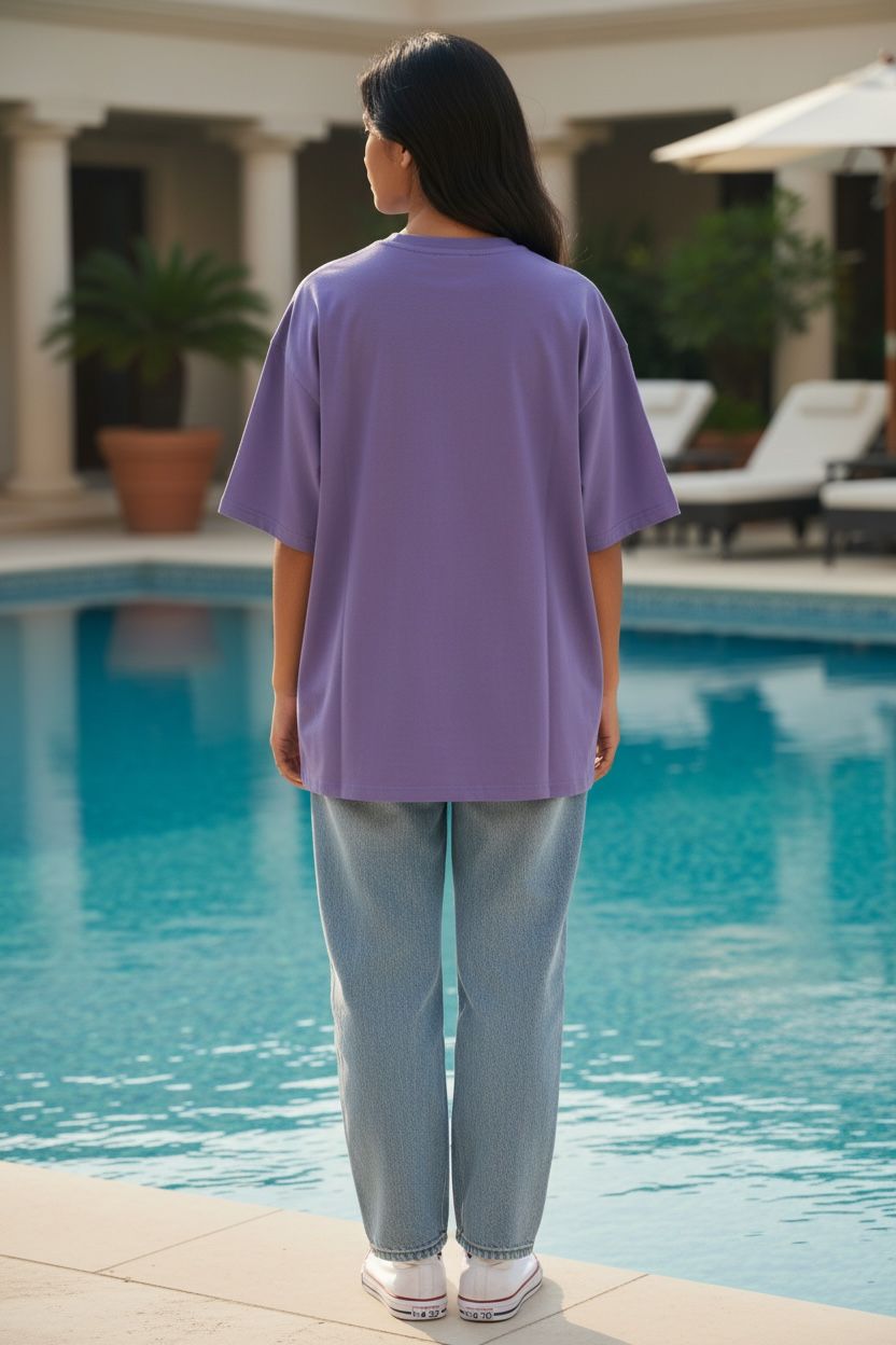 Person wearing a Lavender Tshirt and light blue jeans standing by a pool.