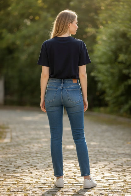 Person wearing blue jeans and a black shirt standing on a cobblestone path with greenery in the background